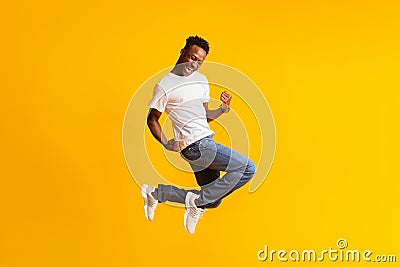 Happy excited young black man jumping over yellow Stock Photo