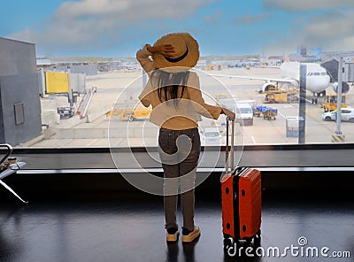 Happy young tourist woman holding the luggage and looking the airplane in the hall room Stock Photo