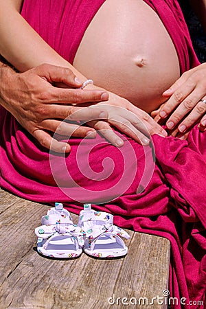 Happy family awaiting baby, love and happiness. Future mom and dad, parents on bench with little unborn baby shoes. Stock Photo
