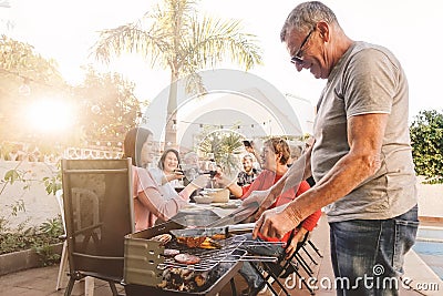 Happy family cheering and toasting with red wine in barbecue party - Chef senior man grilling meat and having fun with parents Stock Photo