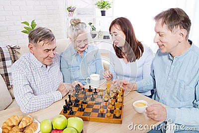 Happy family chess game time at nursing home for elderly. Parents with children have fun talk and leisure. Senior couple Stock Photo