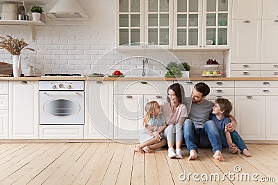 Happy family with children sitting on floor in modern kitchen Stock Photo