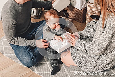 Happy family couple give gifts in the living room, behind the decorated xmas tree, the light give a cozy atmosphere. New Year Stock Photo