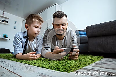 Happy family, Dad and son lying together on the floor, smiling, watching something in a smartphone. The concept of family Stock Photo