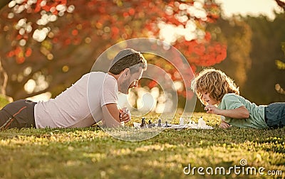 happy family of daddy and son child playing chess on green grass in park outdoor, erudite Stock Photo