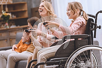 happy family with disabled child in wheelchair playing with joysticks together Stock Photo