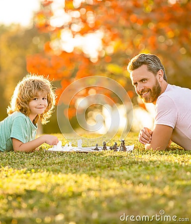 happy family of father man and son child playing chess on green grass in park outdoor, mastermind Stock Photo