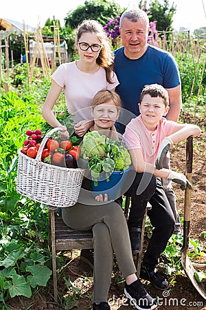 Happy family of four with basket of ripe vegetables on field Stock Photo