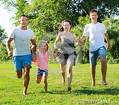 Happy family of four running on grass at summer park Stock Photo