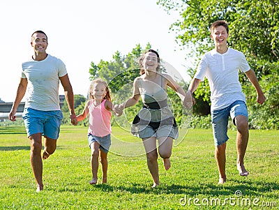 Happy family of four running on grass at summer park Stock Photo