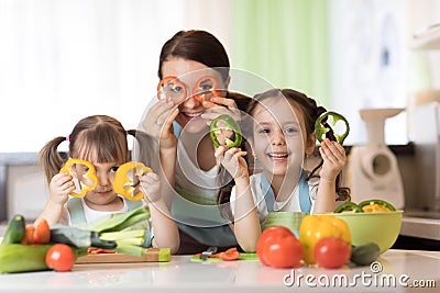 Happy family mother and kids having fun with food vegetables at kitchen holds pepper before their eyes like in glasses Stock Photo