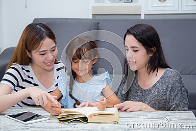 Happy family mother, aunt, freind and daughter teaching read a book at home. Stock Photo