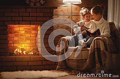 happy family mother and child daughter read book on winter evening near fireplace Stock Photo