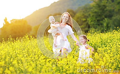 happy family, mother and children little daughter and baby running on meadow with yellow flowers Stock Photo