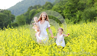 happy family, mother and children little daughter and baby running on meadow with yellow flowers Stock Photo