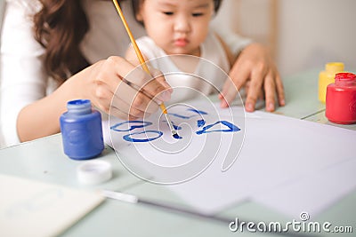 Happy family mother and daughter together paint. Asian woman helps her child girl. Stock Photo