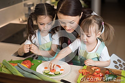 Happy family mother and kids are preparing healthy food, they make funny face with vegetables morsel in the kitchen Stock Photo