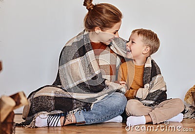 Happy family mother and loving son hug and laugh wrapped in a warm blanket on evening at home Stock Photo