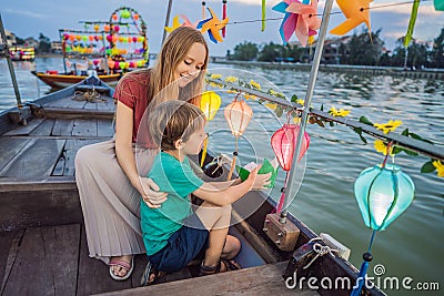 Happy family Mother and son of travelers ride a national boat on background of Hoi An ancient town, Vietnam. Vietnam Stock Photo