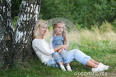 Happy family in nature. Beautiful and happy mother gently hugs her little daughter with blond hair against the background of grass Stock Photo