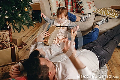 Happy family on new year`s eve spends time at home, man and woman lie on the floor near a decorated Christmas tree Stock Photo