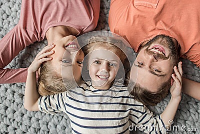 Happy family with one child lying together on grey knitted carpet Stock Photo