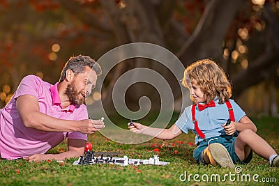 Happy family outdoor. Father and son playing chess in autumn fall garden. Intelligent child, smart kids. Stock Photo