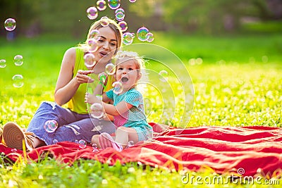 Happy family in park -Female child blows soup foam and make bubbles with her mother in nature. Stock Photo