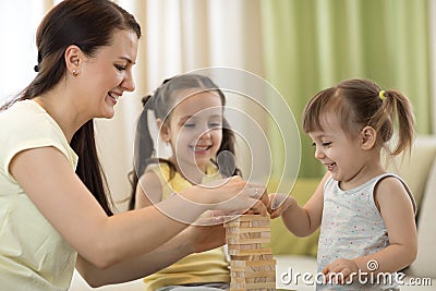 Happy family playing jenga together at home. Mom and daughters having fun in living room. Stock Photo