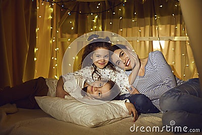 Affectionate mother and two little daughter relaxing in tent in home living room Stock Photo