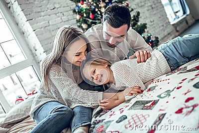 Happy family portrait of mother and girl child laying on cosy bed in festively decorated room with Christmas tree Stock Photo