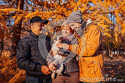 Happy family spending time with pug dog in autumn park. Parents with their son hugging pet. Family values Stock Photo