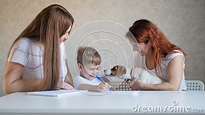 Happy family stays at home. Two women help the boy do school homework. Lesbian couple sitting at the table with their Stock Photo