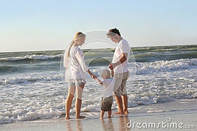 Happy Family of Three People Playing in Ocean While Walking Along Beach Stock Photo