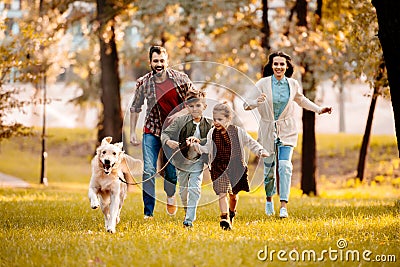 Happy family with two children running after a dog together Stock Photo