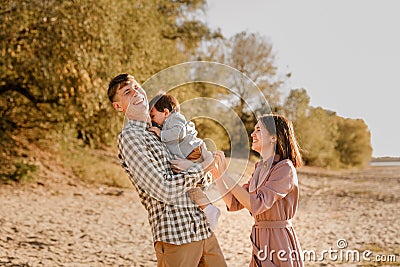 Happy family walking on the road in the park. Father, mother holding baby son on hands and going together. Rear view. Family Ties Stock Photo