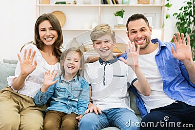 Happy Family Waving Hand Sitting Together On Couch At Home Stock Photo