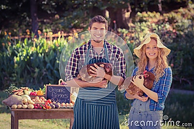 Happy farmers standing at their stall and holding chicken Stock Photo