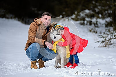 Happy father with daughter on a walk in the woods, girl and husky in yellow scarves, bright clothes in winter Stock Photo