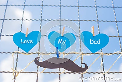 The heart paper written that FATHER and paper mustache on the wire mesh, the blue sky background Stock Photo