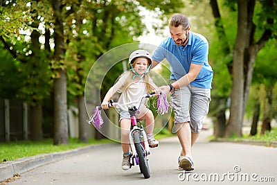 Happy father teaching his little daughter to ride a bicycle. Child learning to ride a bike. Stock Photo