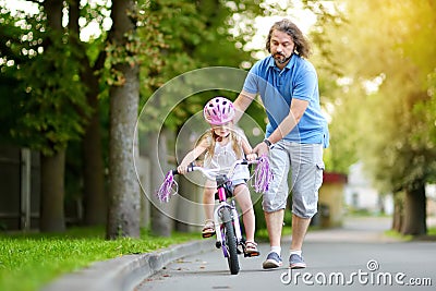 Happy father teaching his little daughter to ride a bicycle. Child learning to ride a bike. Stock Photo