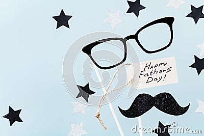 Happy Fathers Day background with greeting tag, glasses, funny moustache and star confetti on table top view. Flat lay style. Stock Photo