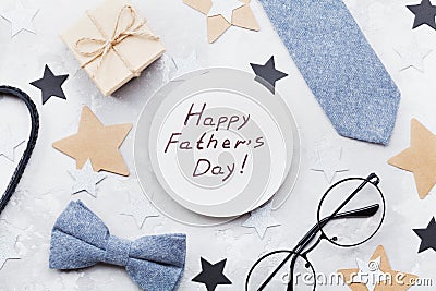 Happy Fathers Day card decorated bowtie, necktie, eyeglasses, gift box and stars on stone table top view in flat lay style. Stock Photo