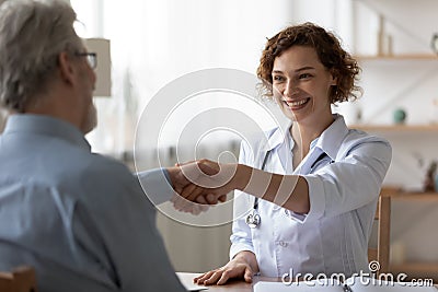 Happy female doctor handshake senior patient at consultation Stock Photo