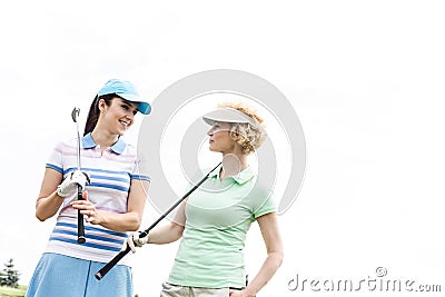 Happy female golfers looking at each other against clear sky Stock Photo