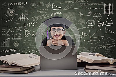 Happy female graduate thinking using laptop at class Stock Photo