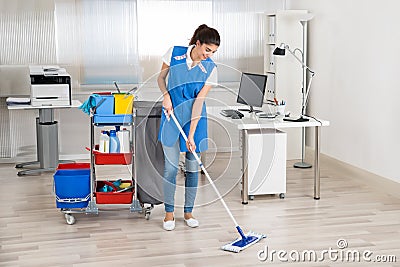 Happy Female Janitor Mopping Floor In Office Stock Photo