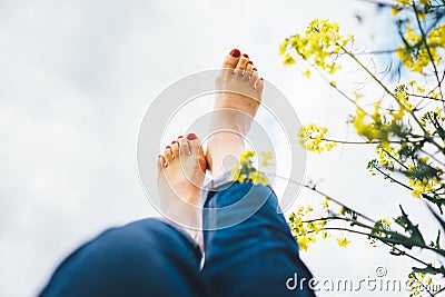 Happy female lying in deep yellow flowers meadow with bright sunny day optical sun beams flares. Happiness in nature concept Legs Stock Photo