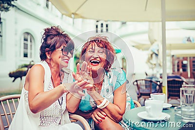 Happy female senior friends laughing and pointing fingers to someone while drinking coffee Stock Photo